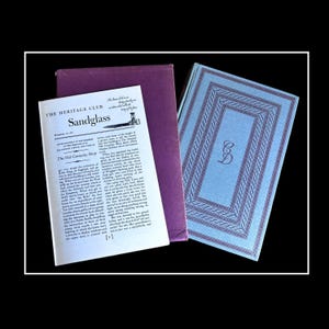May include: A purple and blue book cover with the title "Sandglass" and the text "The Old Curiosity Shop". The book is part of The Heritage Club.