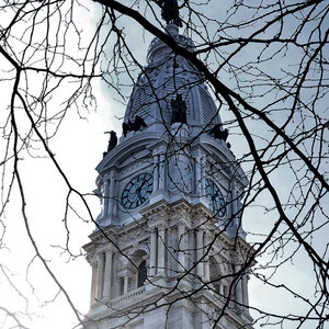 K&ouml;nnte beinhalten: Ein wei&szlig;er Uhrturm mit einem sichtbaren Zifferblatt an der Vorderseite. Der Turm ist teilweise von kahlen &Auml;sten verdeckt.