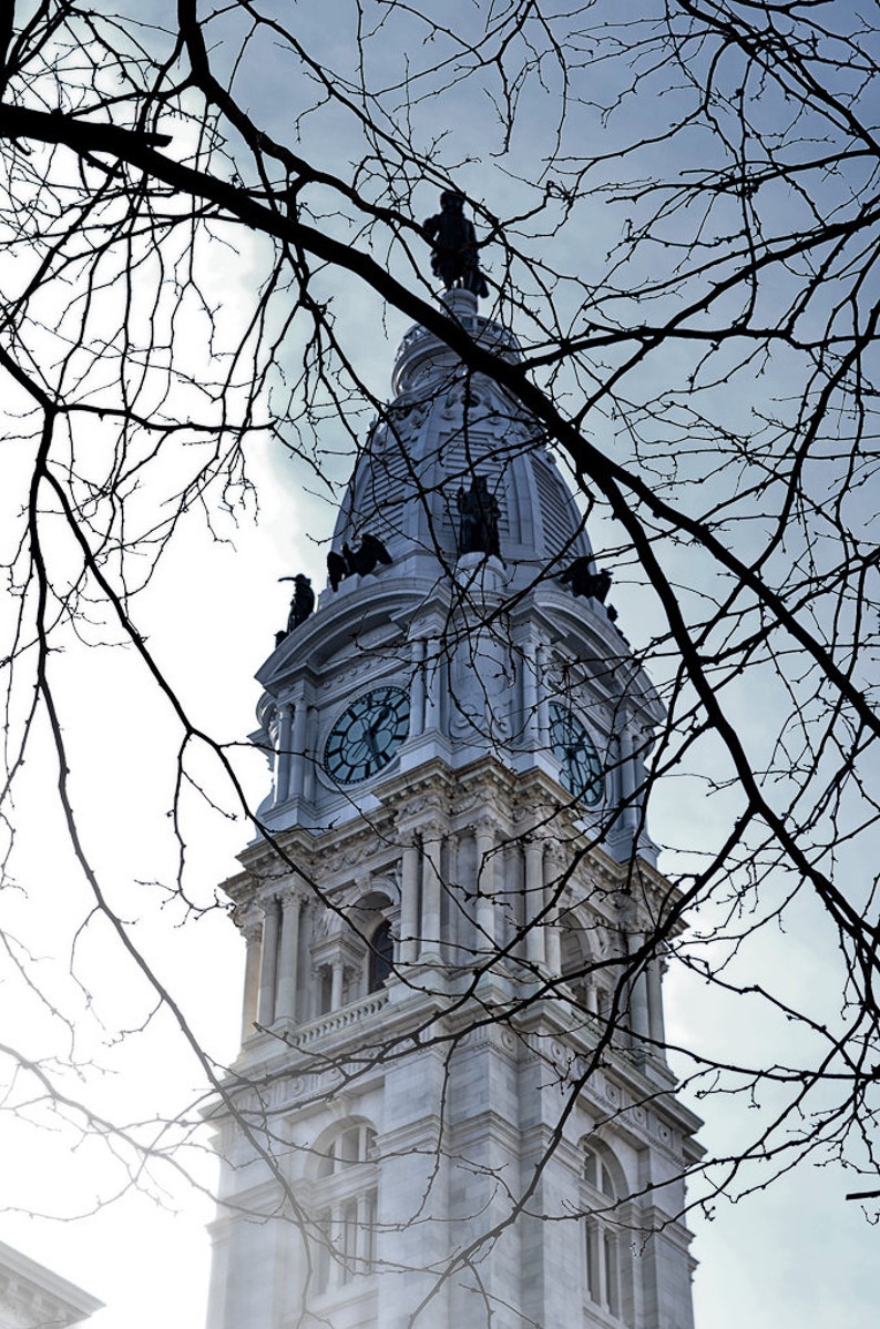 K&ouml;nnte beinhalten: Ein wei&szlig;er Uhrturm mit einem sichtbaren Zifferblatt an der Vorderseite. Der Turm ist teilweise von kahlen &Auml;sten verdeckt.