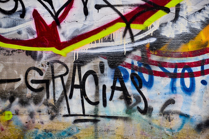 K&ouml;nnte beinhalten: Eine Nahaufnahme einer mit Graffiti bespr&uuml;hten Wand mit dem Wort "GRACIAS" in schwarzer Farbe. Die Wand ist auch mit roter, gelber, blauer und wei&szlig;er Farbe bedeckt.