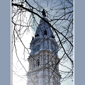 K&ouml;nnte beinhalten: Ein Blick auf den Uhrturm des Philadelphia City Hall, gesehen durch kahle &Auml;ste eines Baumes. Das Zifferblatt der Uhr ist sichtbar, und der Turm ist mit einer Statue gekr&ouml;nt.