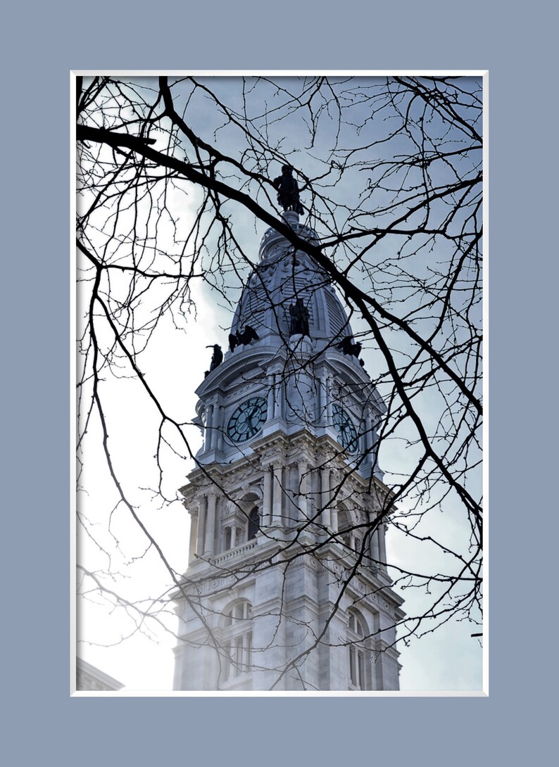K&ouml;nnte beinhalten: Ein Blick auf den Uhrturm des Philadelphia City Hall, gesehen durch kahle &Auml;ste eines Baumes. Das Zifferblatt der Uhr ist sichtbar, und der Turm ist mit einer Statue gekr&ouml;nt.