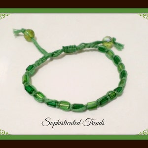 May include: A green bracelet with green glass beads and a green cord. The bracelet is tied with a knot.