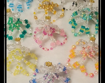 Op de afbeelding: Negen kralenengel-versieringen in verschillende kleuren, waaronder blauw, geel, groen, roze, wit en iriserend. Elke engel heeft een kralenkroon en een kralenjurk.