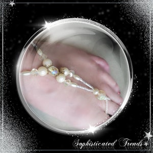 Op de afbeelding: Een delicate witte en gouden kralen voetsieraden met kristallen accenten. De sieraden worden gedragen op een voet met zichtbare tenen.