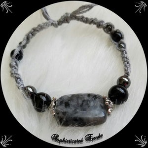 May include: Gray braided bracelet with black and silver beads and a large gray and black gemstone.
