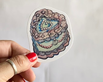 Può includere: Un adesivo di una torta colorata a più strati con una forma di cuore al centro. La torta è decorata con spirali, punti e perle.