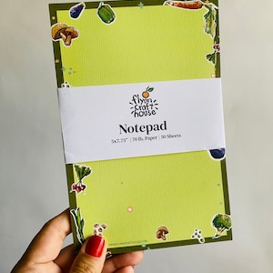 May include: A green notepad with a white border and a green and white border. The notepad has a variety of vegetable illustrations on the front. The text on the front reads "Flynn Craft House Notepad 5x7.75" 70 lb. Paper | 50 Sheets www.flynncrafthouse.com"