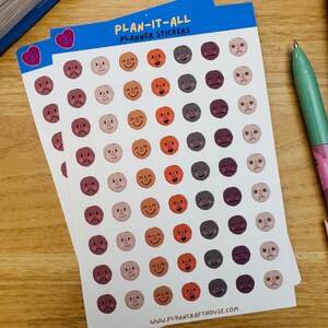 May include: Two sheets of planner stickers featuring rows of small, hand-drawn circular faces with various expressions. The blue header reads PLAN-IT-ALL PLANNER STICKERS. The bottom includes the text WWW.FLYNNCRAFTHOUSE.COM. The faces are in shades of orange, brown, and grey.