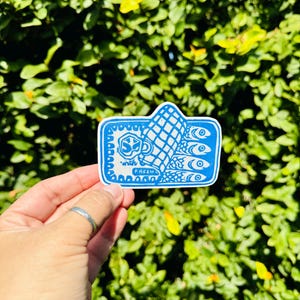 Op de afbeelding: Een blauwe en witte sticker met een hand die een vis vasthoudt. De hand houdt een vis vast met de tekst "with fresh" erop.