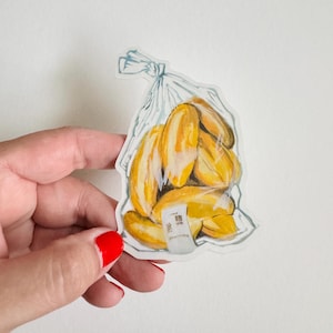 Op de afbeelding: Een aquarelillustratie van een plastic zak gevuld met gele bananen. De zak heeft een wit label met Japanse tekst.