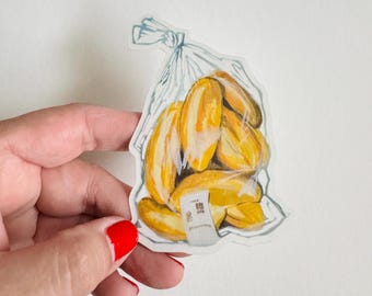 Pode incluir: Uma ilustração em aquarela de uma sacola plástica cheia de bananas amarelas. A sacola tem um rótulo branco com texto japonês.