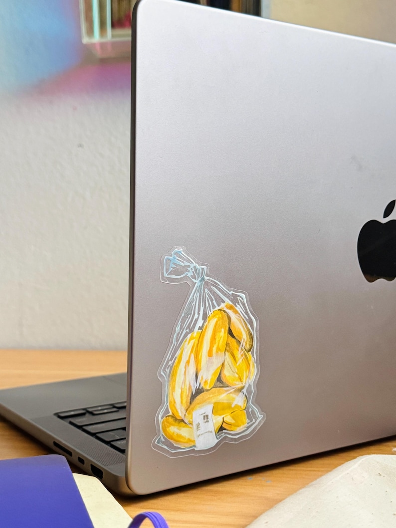 Op de afbeelding: Een doorzichtige plastic zak met een tros gele bananen erin. De zak zit op een zilveren laptop.