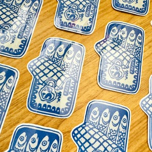 Op de afbeelding: Een set blauwe en witte stickers met een gestileerde illustratie van een blikje sardines. Het blikje is open en de sardines zijn zichtbaar in het blikje. De tekst "Fresh With A Twist" is op het blikje gedrukt.