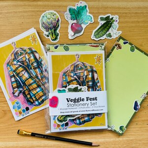 May include: A set of stationery featuring a yellow background with a plaid shirt design and a green background with a vegetable design. The set includes a 150-page notepad, 3 postcards, and 3 vinyl stickers. The text on the packaging reads "Veggie Fest Stationery Set".
