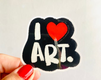 Puede incluir: Una pegatina en blanco y negro con el texto "I love art." en letras blancas. Un corazón rojo está en el medio de la pegatina. La pegatina tiene un borde blanco.