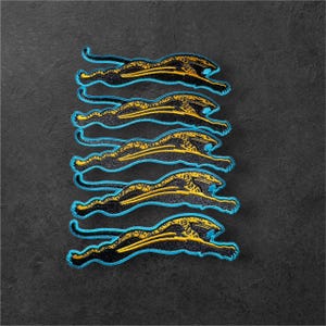 May include: A set of five embroidered patches, each featuring a stylized leaping jaguar in black and yellow thread with a bright cyan blue border. The patches are arranged in a vertical column, showcasing the same feline design.