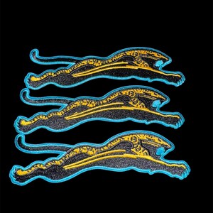 May include: Three identical embroidered patches, each depicting a stylized leaping jaguar in profile. The design features a black body with yellow spotted patterns, outlined in a vibrant light blue thread against a dark background.