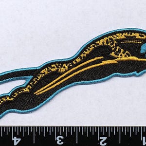 May include: Black and gold embroidered patch of a leaping panther with a blue outline. The panther is facing right and has a stylized design.