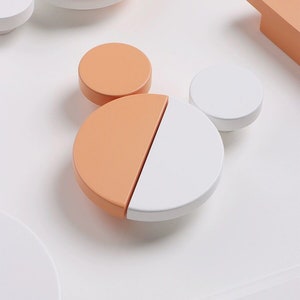 Peut inclure: Un ensemble de cinq boutons de porte de style moderne. Les boutons sont en bois et peints en blanc et pêche.