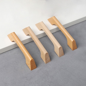 Puede incluir: Cuatro tiradores de armario de madera en varios tonos de marrón. Los tiradores tienen todos la misma forma, con una parte superior curva y una parte inferior plana.