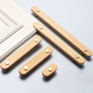 Peut inclure: Cinq poignées de tiroir en bois avec des boutons en laiton de différentes tailles. Les poignées sont en bois clair et ont une finition naturelle.