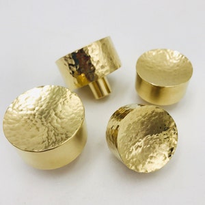 May include: Four gold-toned hammered metal cabinet knobs. The knobs are round and have a slightly domed shape.