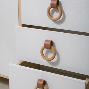 May include: White chest of drawers with four drawers. Each drawer has a wooden ring pull with a brown leather strap.