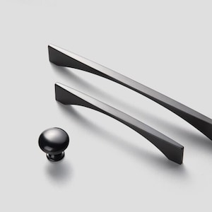 Puede incluir: Dos tiradores de armario de metal negro con un diseño curvo y un pomo de metal negro.