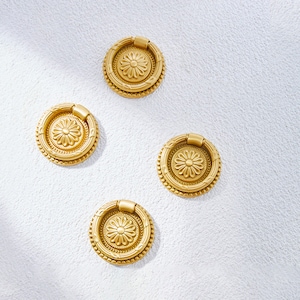 May include: Four gold-toned round cabinet knobs with a decorative floral design. Each knob has a ring pull.