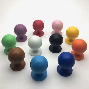 May include: Assortment of 12 colourful round cabinet knobs with a smooth finish. The knobs are in various colours, including green, blue, brown, orange, yellow, pink, red, purple, white, and black.