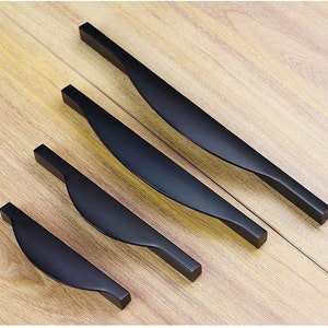 Puede incluir: Cuatro tiradores de armario de metal negro con un diseño curvo. Los tiradores están dispuestos en orden descendente de tamaño.