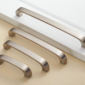 May include: Four brushed nickel cabinet pulls in different sizes. The pulls are all the same style, with a rounded rectangular shape and a slight curve.