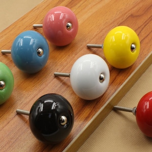 Peut inclure: Assortiment de dix boutons de cabinet en céramique de différentes couleurs, notamment vert, bleu, blanc, noir, jaune et rouge. Chaque bouton a une forme ronde et un petit accent métallique au centre.