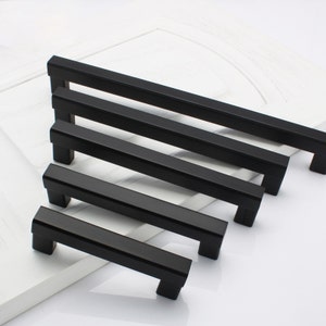 May include: Five black metal cabinet pulls of varying lengths. The pulls have a rectangular shape with squared edges.