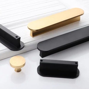 May include: Four cabinet pulls in two different styles. Two are long and rectangular with rounded ends, one is gold and one is black. The other two are round and black with a small knob on top.