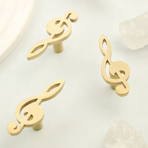 以下が含まれることがあります： トレブル・クレフの形をした金色の金属製のキャビネットノブが3つあります。