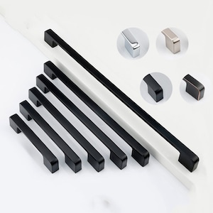 May include: A set of six black cabinet pulls with a rectangular shape and rounded edges. The pulls are arranged in a staggered pattern on a white surface.