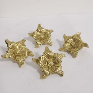 Op de afbeelding: Vier goudkleurige metalen bloemvormige decoratieve versieringen met een verhoogd midden.