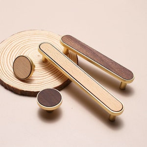 Peut inclure: Quatre boutons et poignées de cabinet avec une finition en bois et en laiton. Deux boutons ronds et deux poignées rectangulaires. Les boutons et les poignées ont un centre en bois clair avec une bordure en bois foncé et une bordure en laiton.