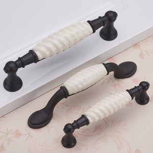 Puede incluir: Tres pomos de armario de cerámica blanca y negra con un diseño retorcido. Los pomos son de diferentes tamaños y tienen una base de metal negro.