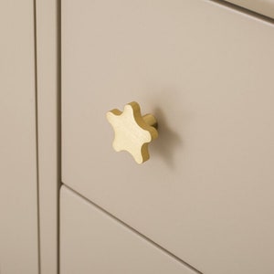 Puede incluir: Un pomo de armario en forma de estrella dorada con acabado cepillado.