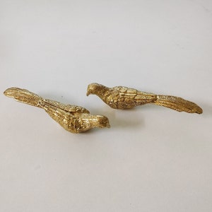 以下が含まれることがあります： 羽根が細かく表現された金色の鳥の置物2つ。鳥は反対方向を向いており、長く細い尾を持っている。
