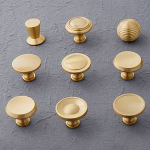 Könnte beinhalten: Sortiment aus zehn goldenen Schrankknöpfen in verschiedenen Stilen, darunter runde, kuppelförmige und zylindrische Formen.