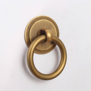 May include: A brass ring pull cabinet door handle with a round base. The handle is a single ring with a smooth, polished finish.