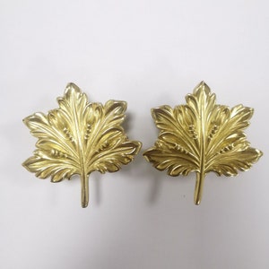 May include: Two gold-coloured metal leaf-shaped decorative pieces. Each piece is a stylised representation of a maple leaf with intricate details.