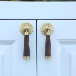 May include: Two brass cabinet knobs with a dark wood handle. The knobs have a circular base with a decorative ring around the edge.