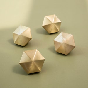 Könnte beinhalten: Vier goldfarbene, geometrische, sechseckige Schubladenknöpfe mit gebürsteter Oberfläche.