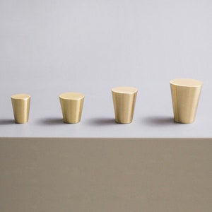 Peut inclure: Quatre boutons de cabinet en laiton de différentes tailles. Les boutons sont tous en forme de cône et ont une finition lisse et polie.