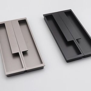 May include: Two drawer pulls, one in a brushed nickel finish and one in black. Both pulls are rectangular with a recessed handle.